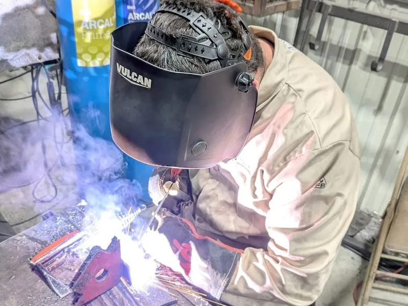 A student welding under a bright arc in a welding helmet.