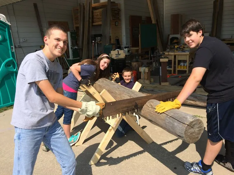 Students sawing a log together on a sawbuck.